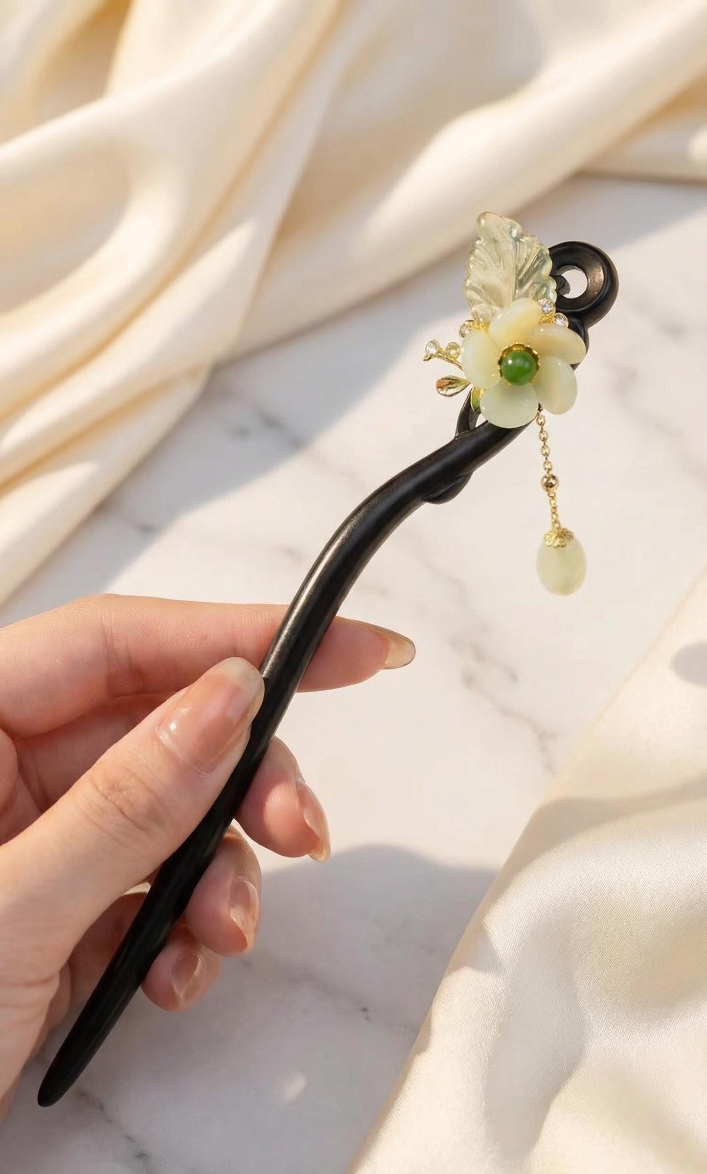Decorative hair stick with floral design held by a hand against a soft fabric background