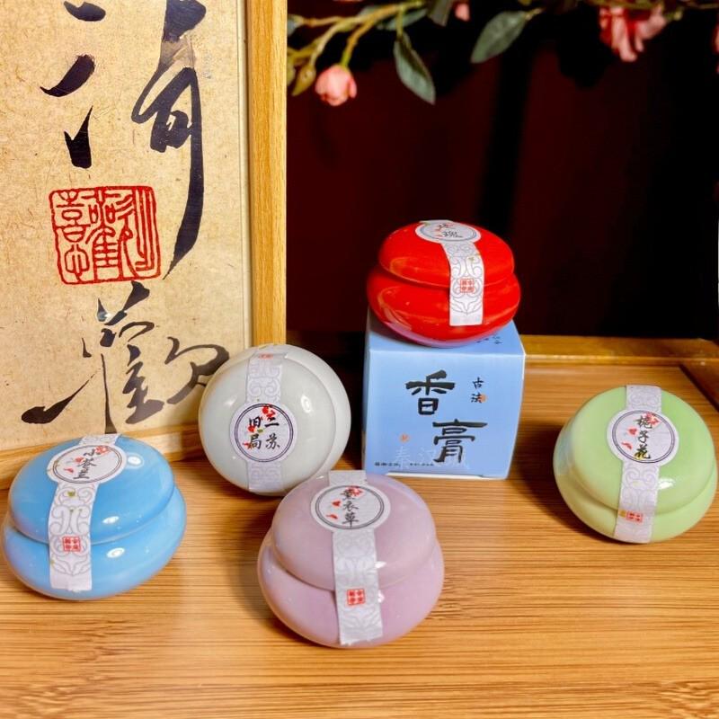 Set of small containers with colorful lids on a wooden surface, with calligraphy in the background.