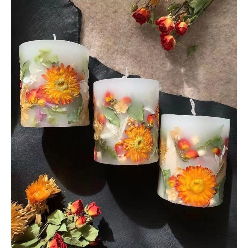 Three floral candles on a dark surface with dried flowers around