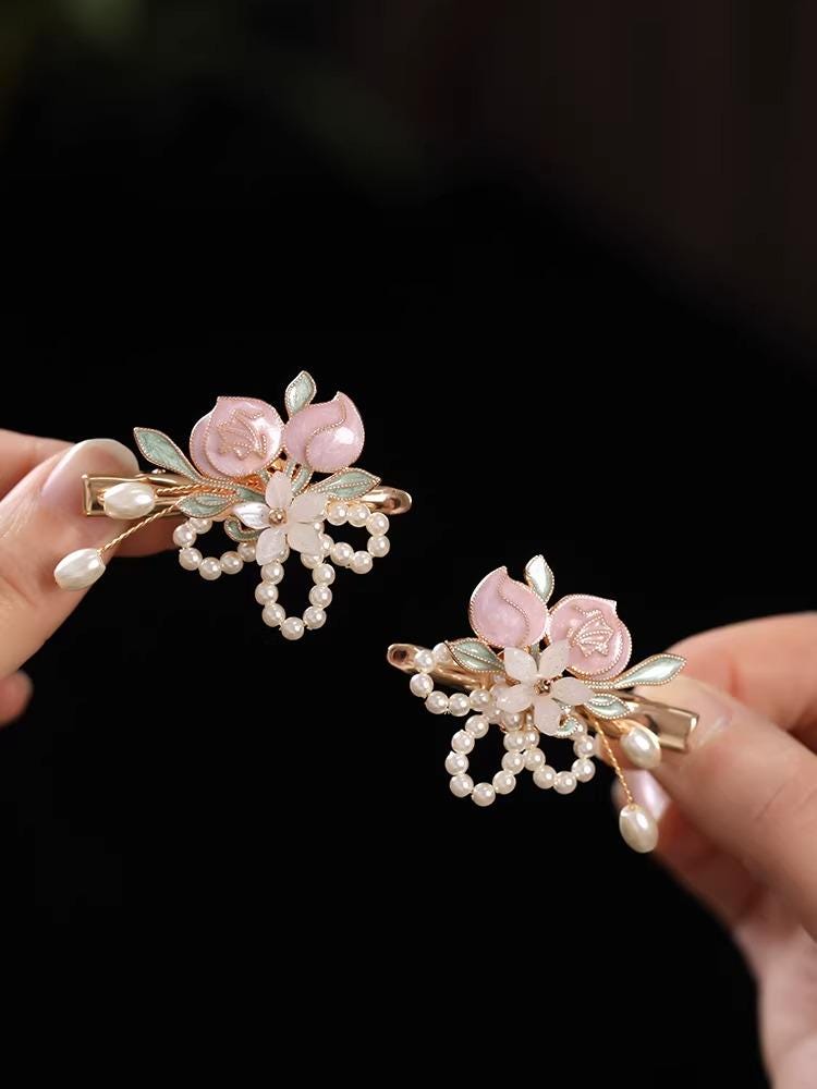 Two decorative hair clips with floral designs held by a hand against a black background