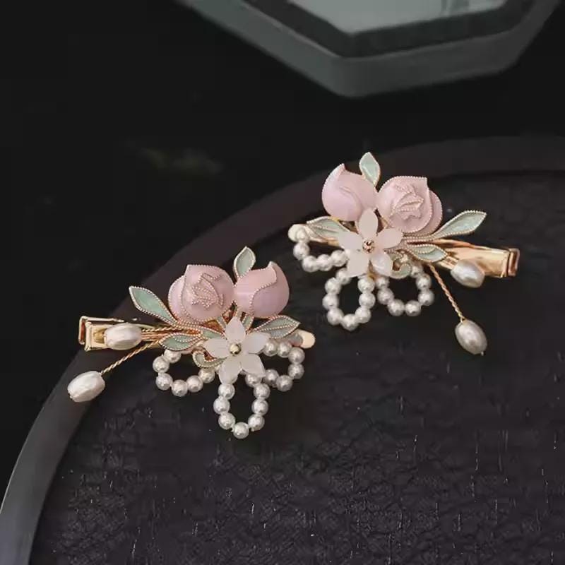 Two decorative hair pins with floral and pearl details on a dark surface.