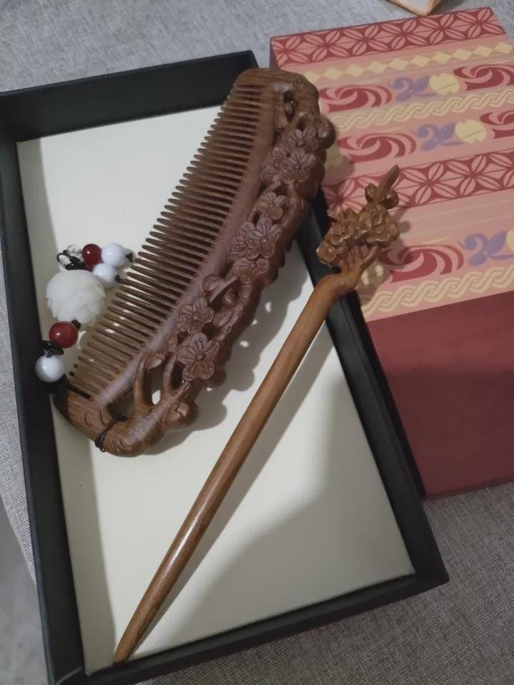 Wooden comb and hairpin on a textured surface with a decorative box in the background.