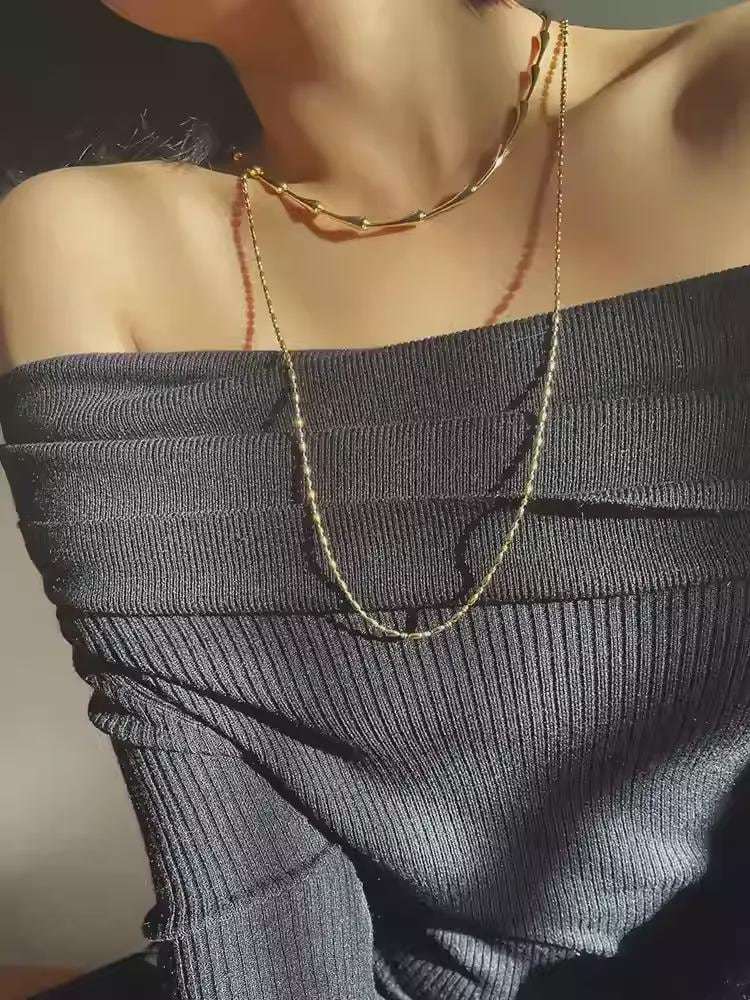 Gold necklace on a person wearing a dark gray off-shoulder top.