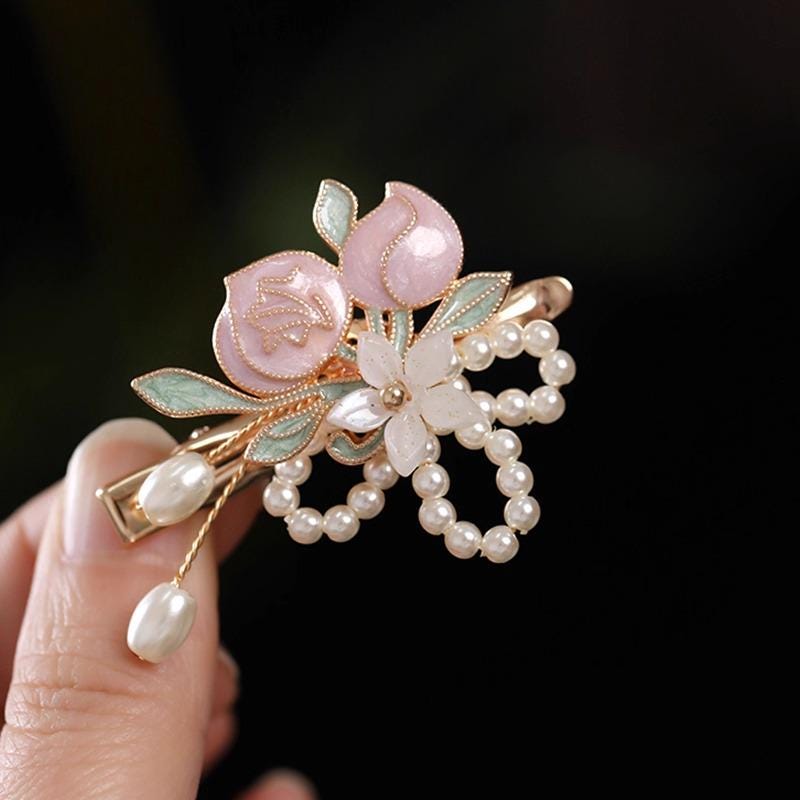 Decorative hair clip with floral design and pearls held by a hand against a dark background
