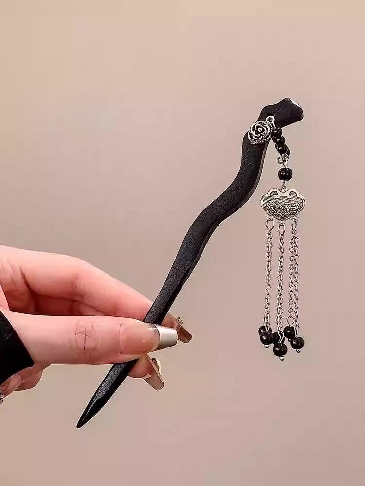 hair stick with black ribbon and silver embellishments held by a hand against a beige background