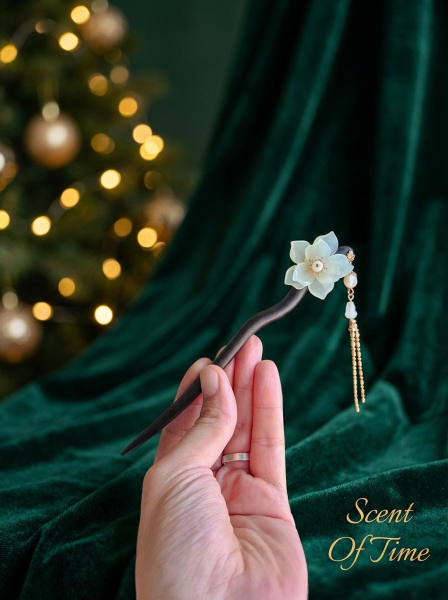 Hand holding a decorative hairpin with floral design against a green curtain background.