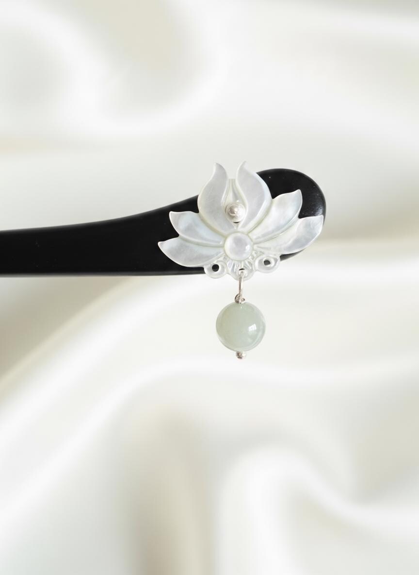 Decorative hairpin with white floral design and green bead on a white background