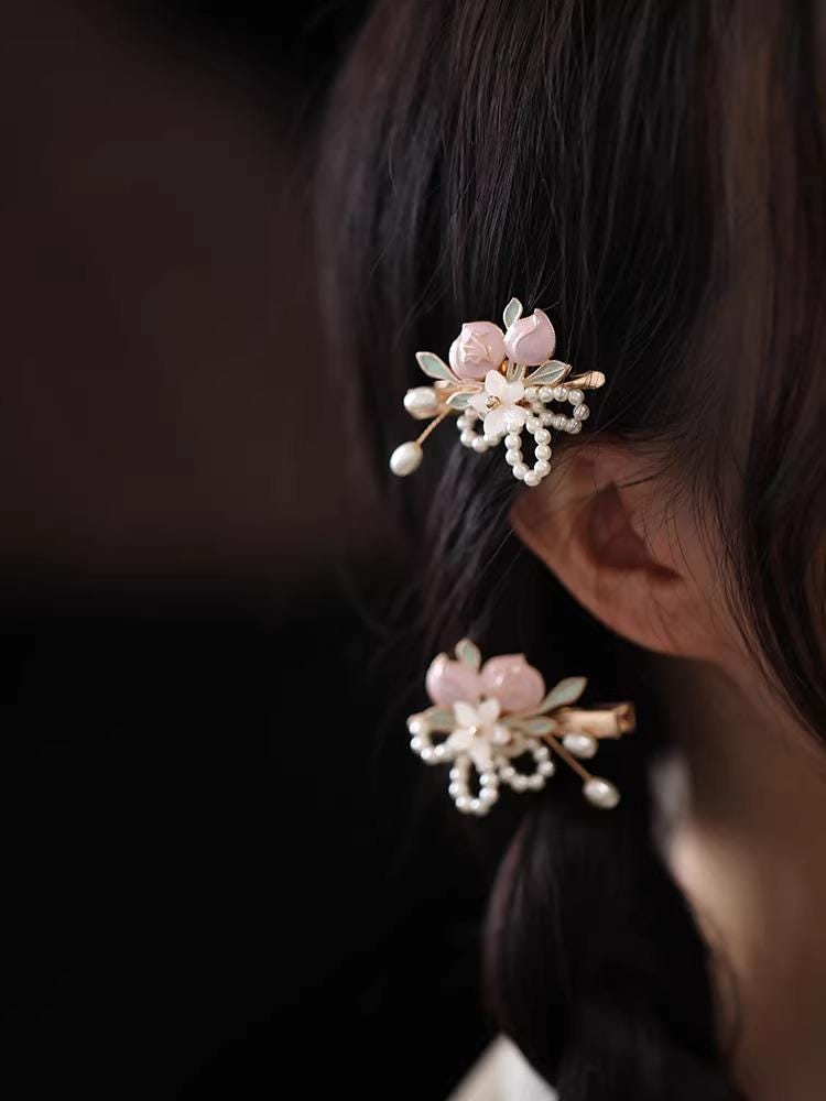 Close-up of a person wearing floral hairpins with pink flowers and pearl details.