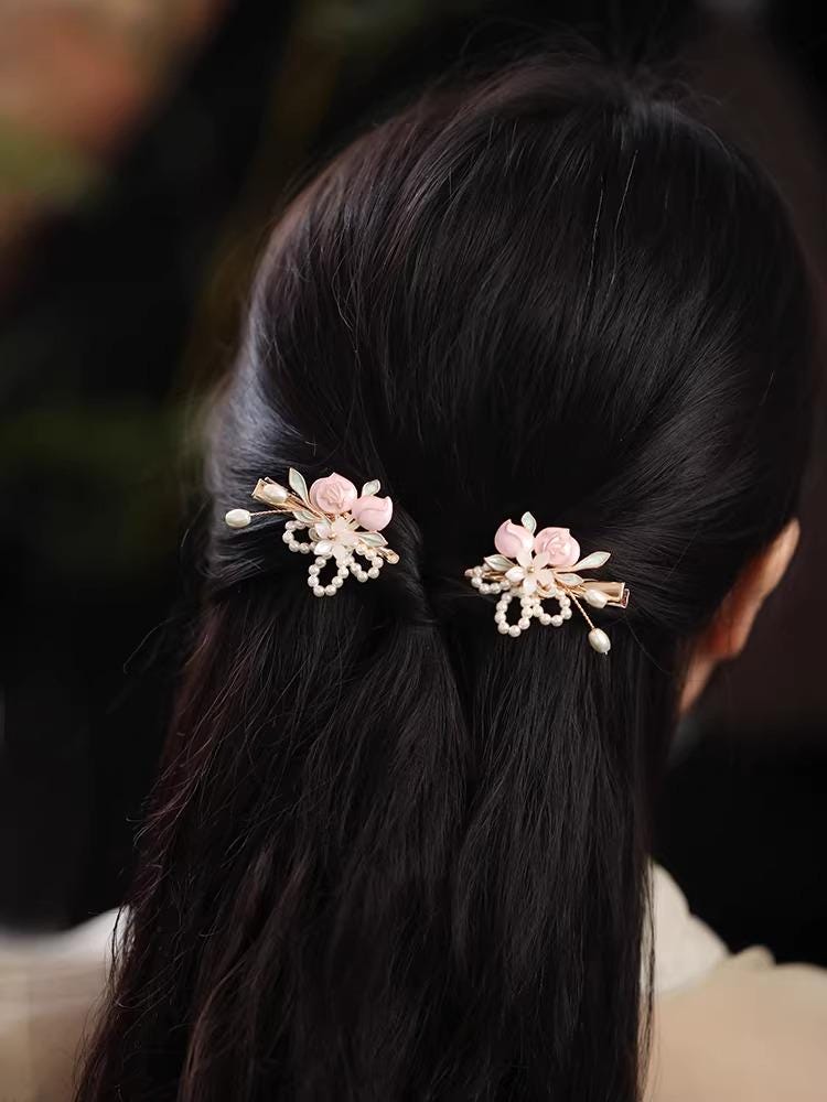 Black hair with decorative hairpins featuring flowers and pearls against a dark background