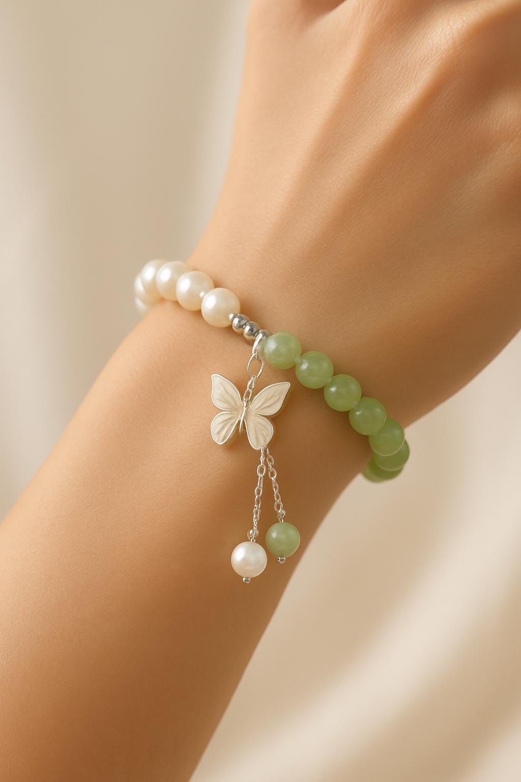 Bracelet with green beads, pearls, and a butterfly charm on a wrist against a neutral background