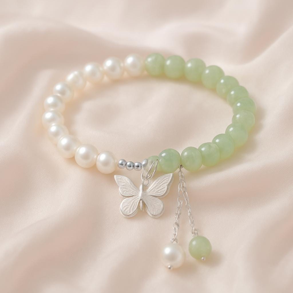 Bracelet with pearls and green beads featuring a butterfly charm on a soft pink background