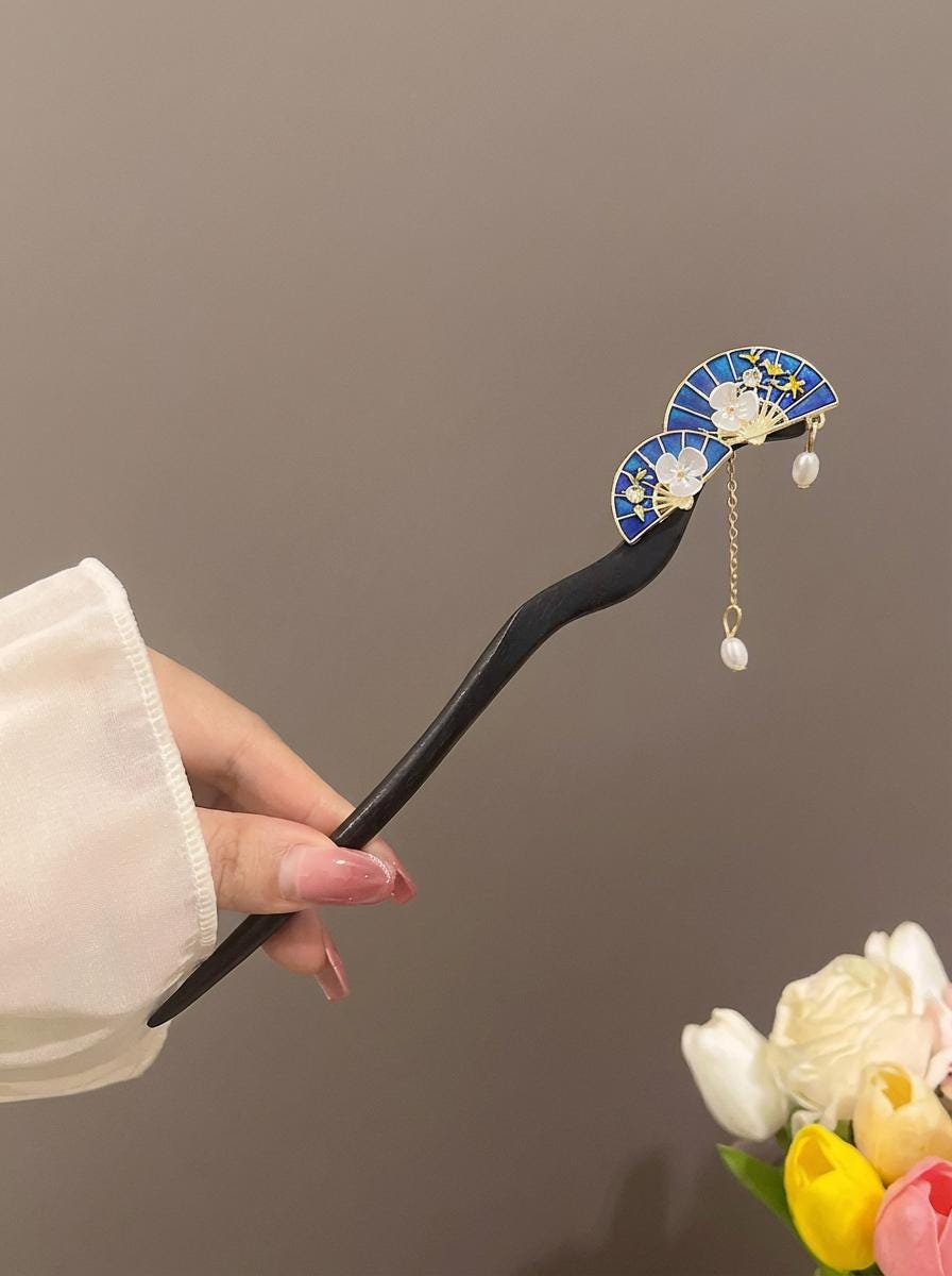 Hairpin with decorative elements held by a hand against a neutral background