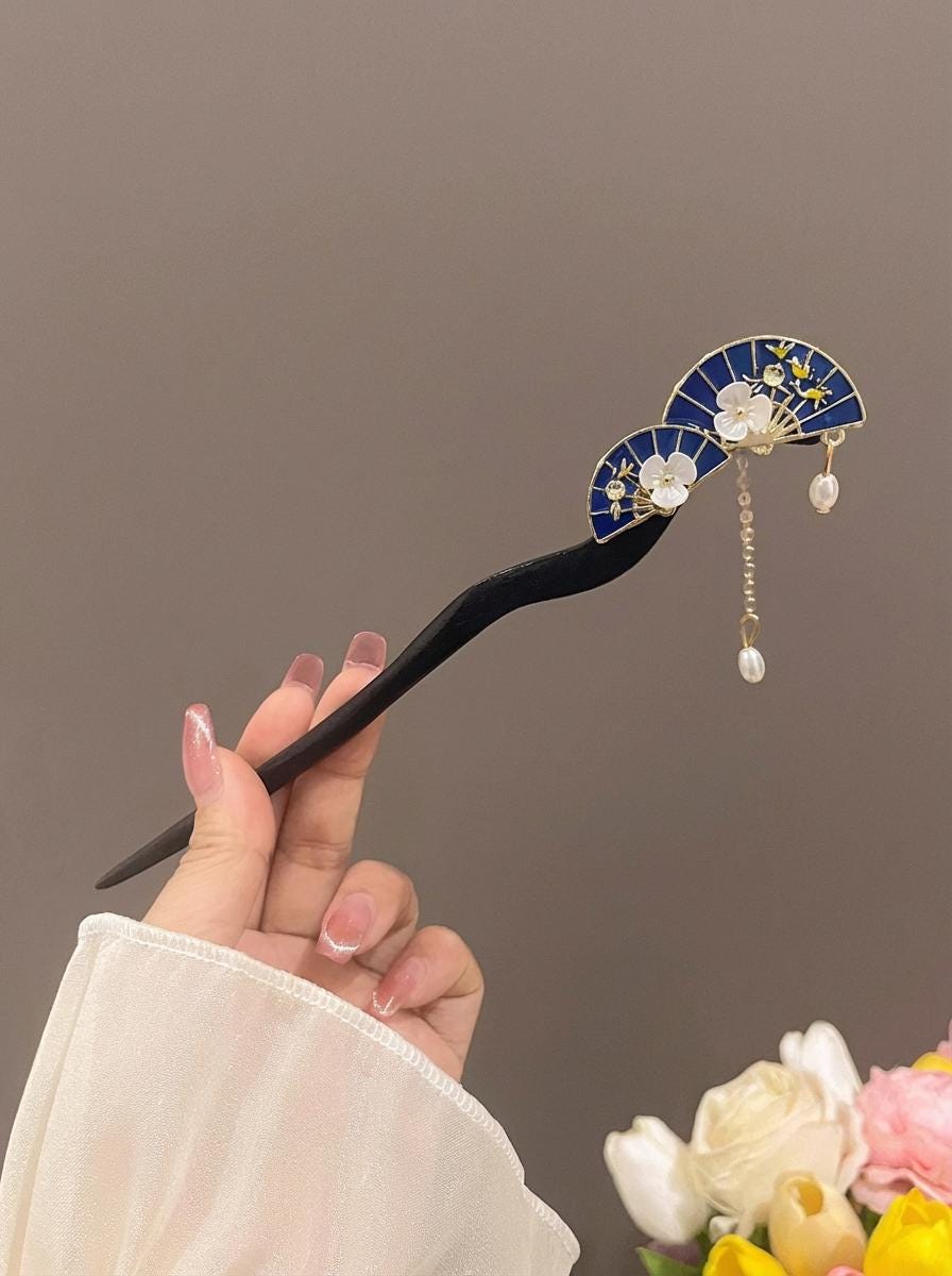 Hand holding a black hairpin with decorative elements against a neutral background