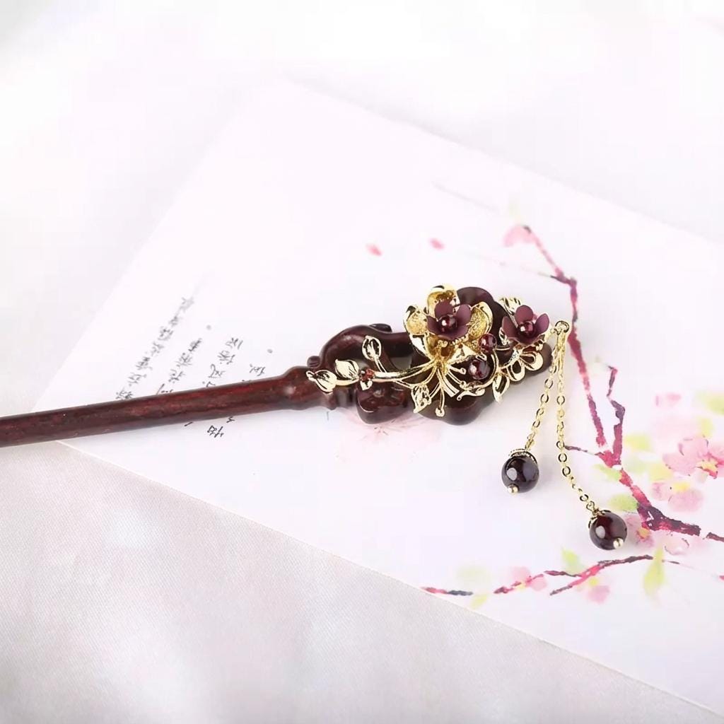 Decorative hair stick with gold accents and dark beads on a white background