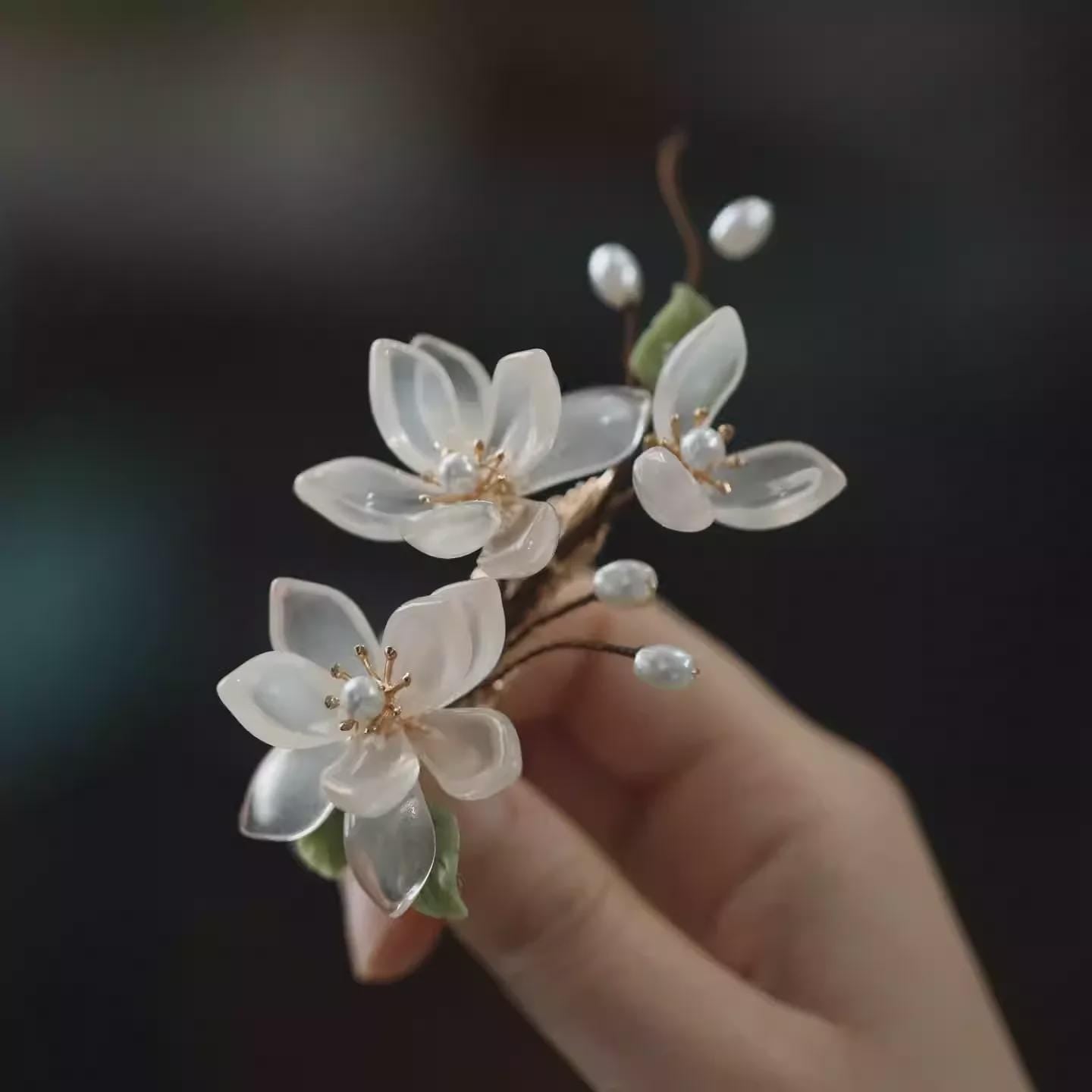 Hand holding a delicate floral hair accessory with clear flowers and pearls against a dark background