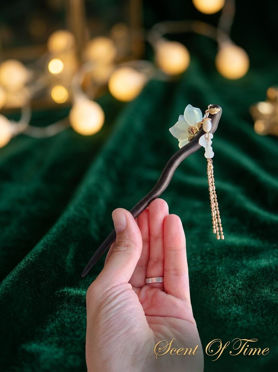 Hand holding a decorative hairpin with floral elements against a green fabric background.