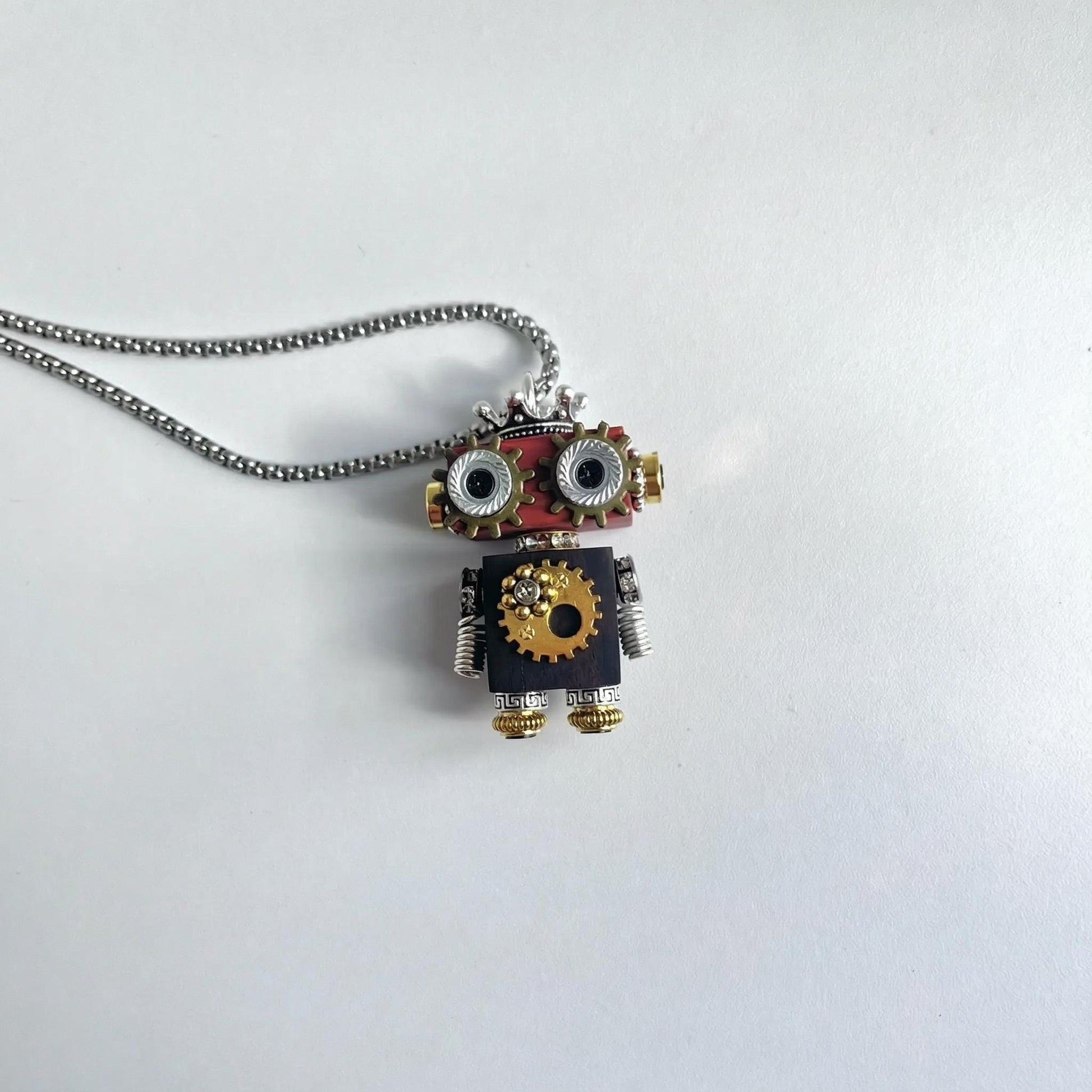 Robot-shaped pendant on a chain against a white background