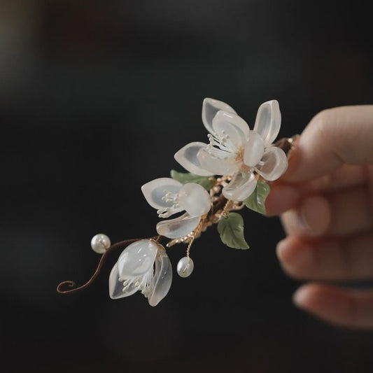 Delicate floral hairpiece held by a hand against a dark background