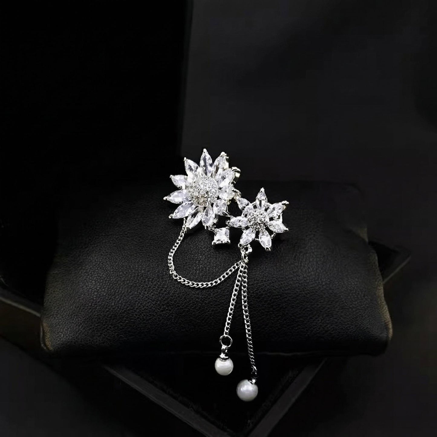 Silver floral brooch with chain and beads on a dark background