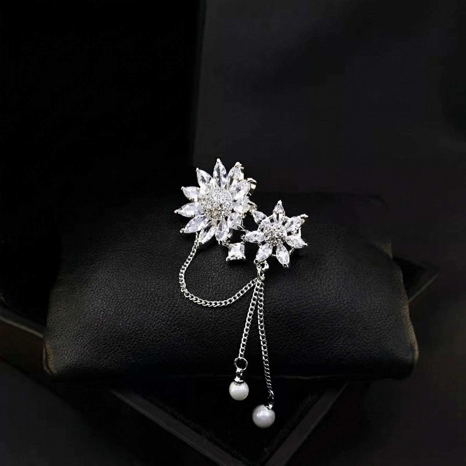 Silver floral brooch with chain and beads on a dark background