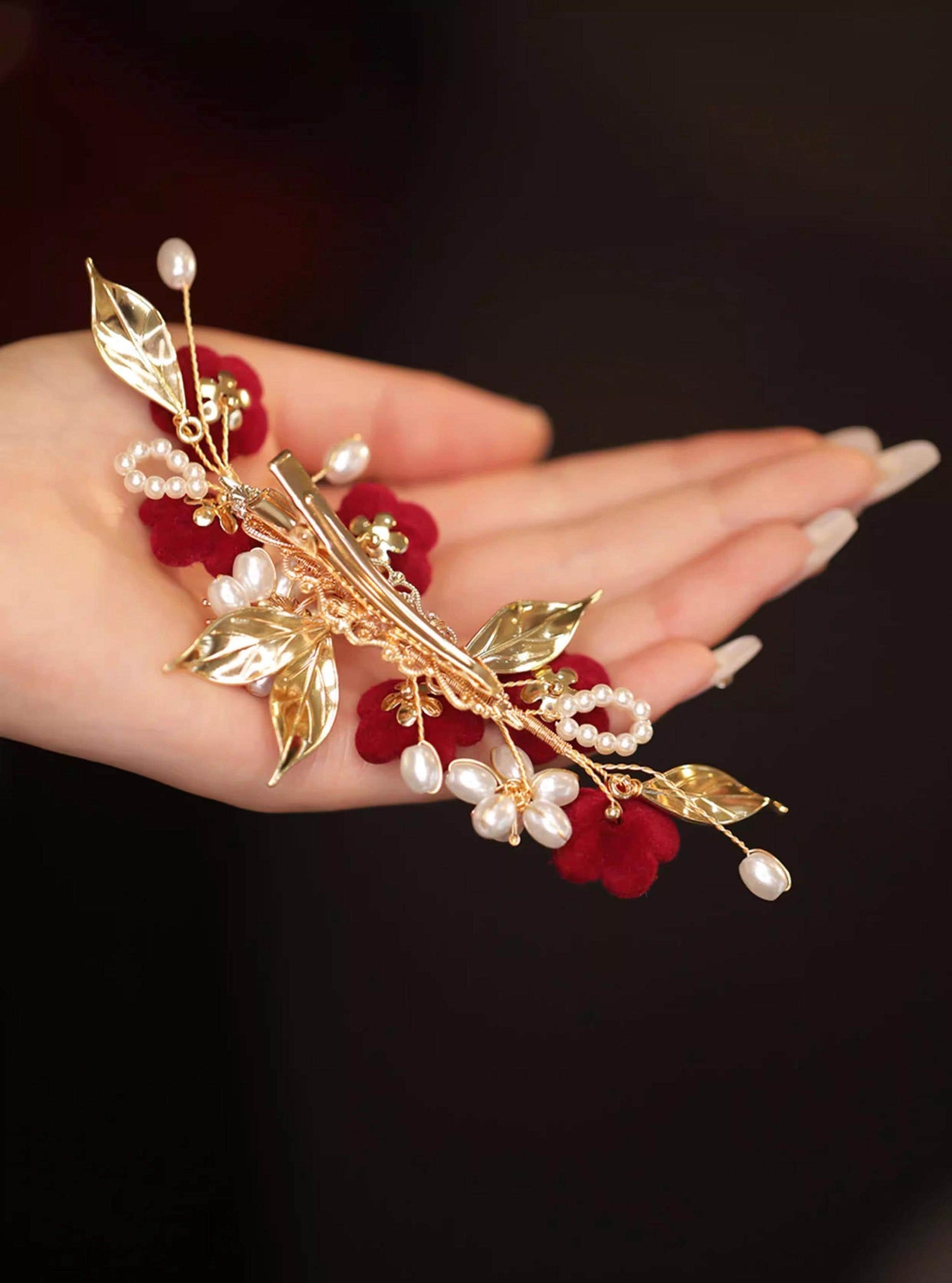 Gold leaf and pearl hair accessory held in a hand against a dark background