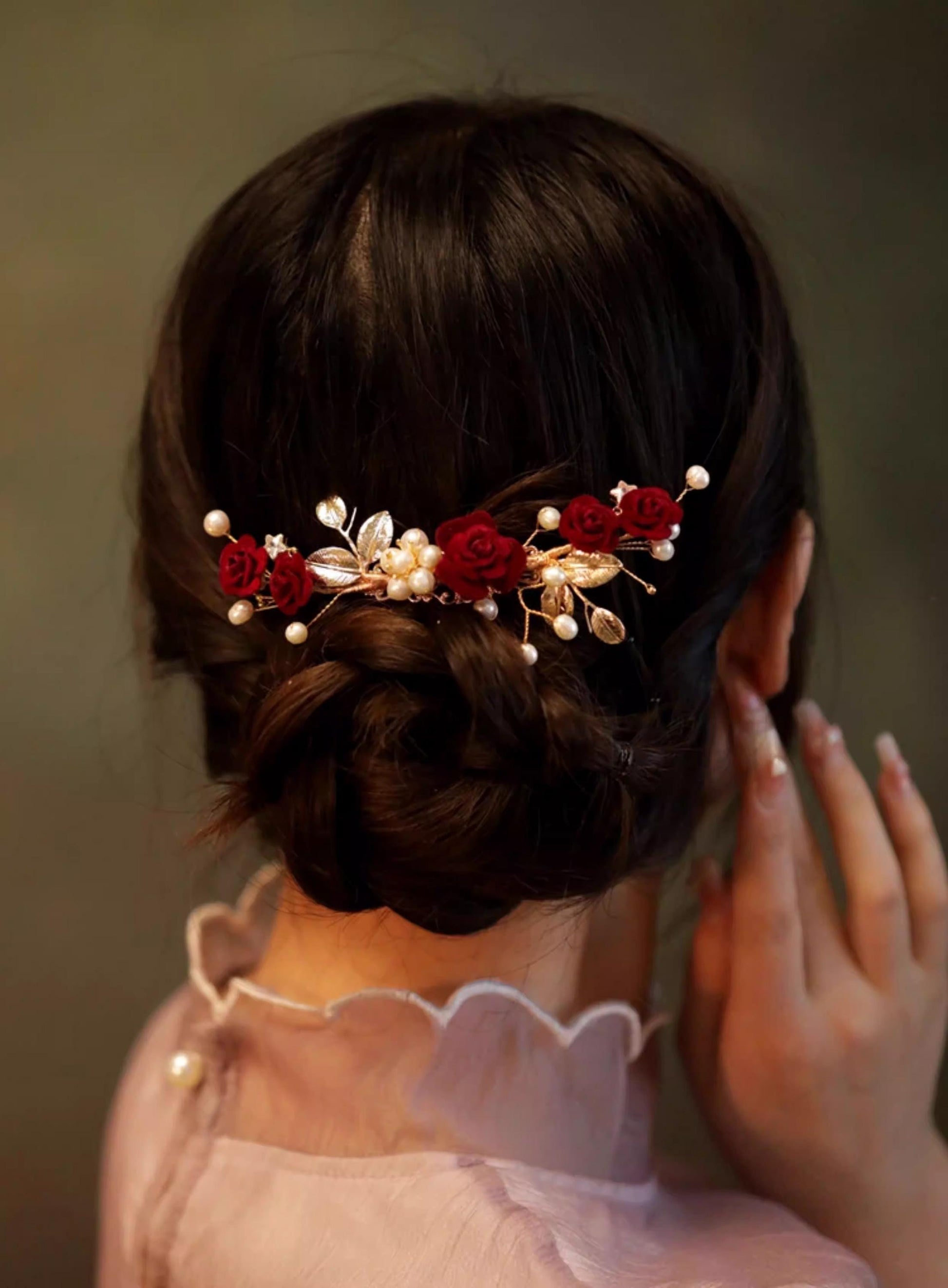 Person wearing a decorative hairpiece with red flowers and pearls against a neutral background
