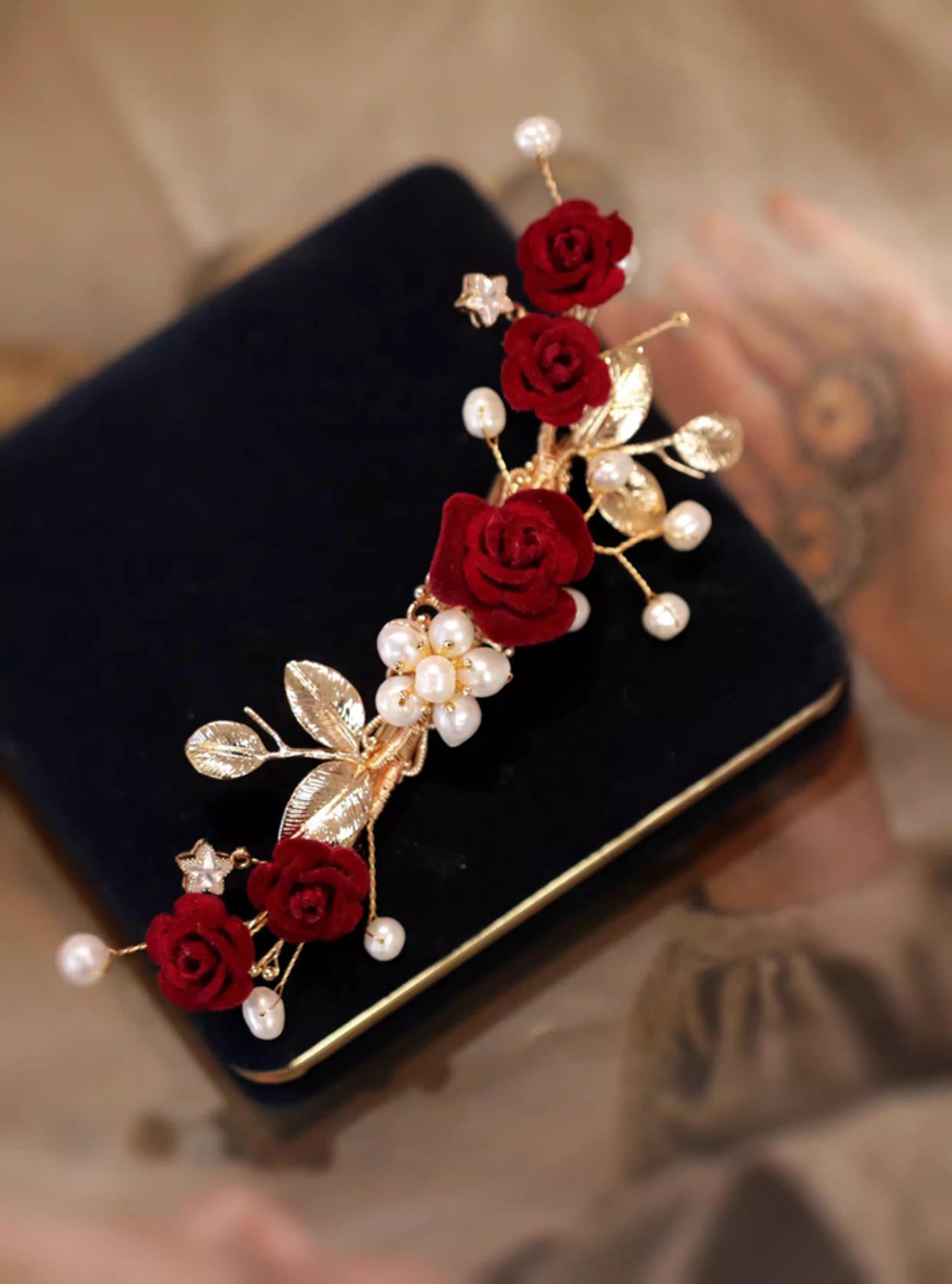 Decorative hair clip with red roses and pearls on a black velvet surface