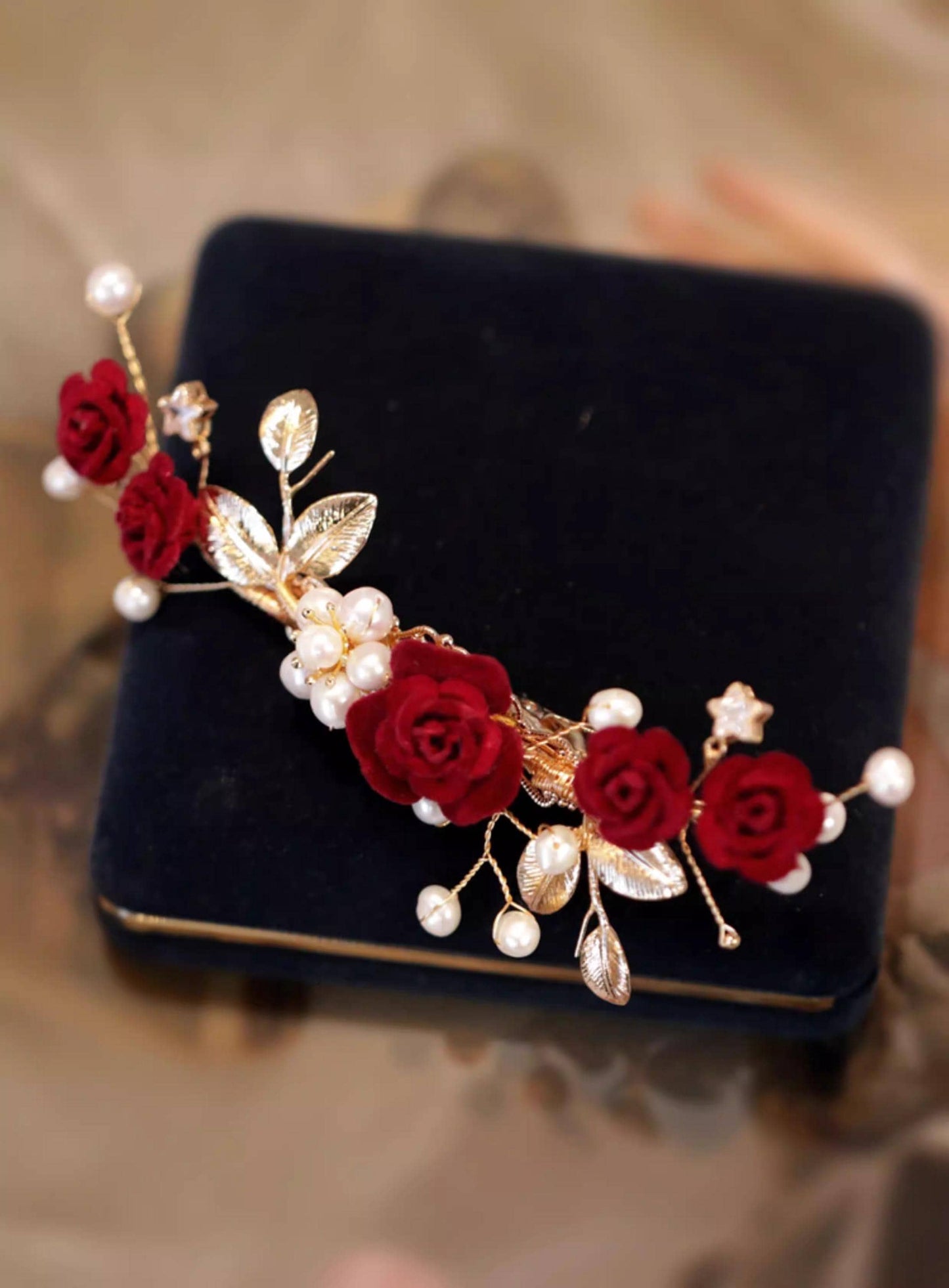 Decorative hairpiece with red flowers and gold leaves on a black velvet cushion.