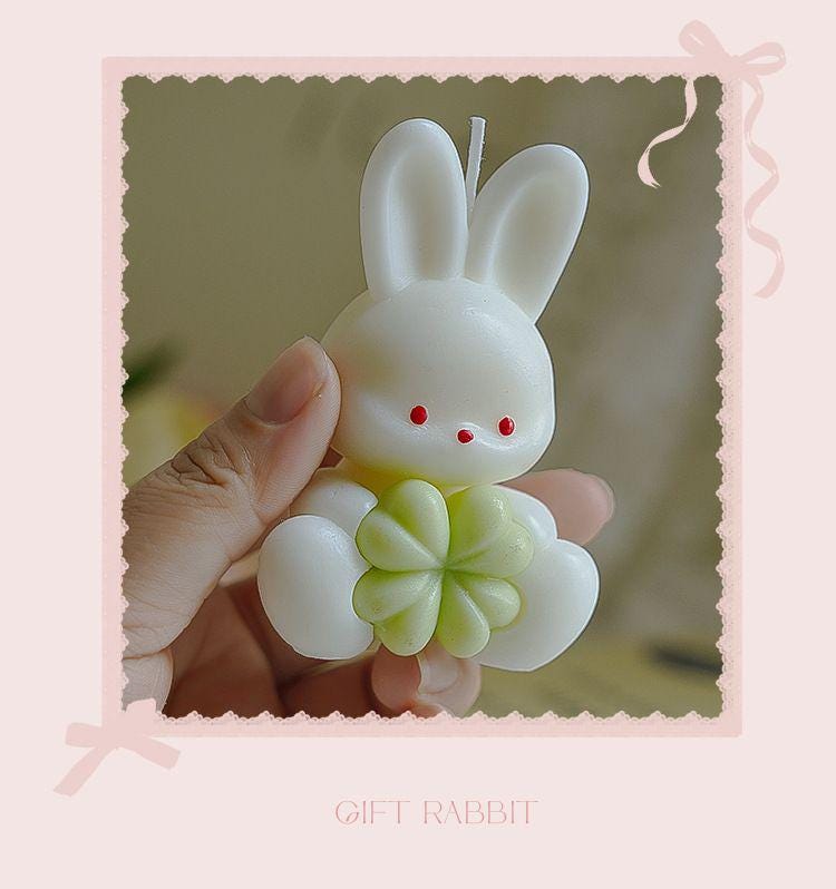 Candle shaped like a rabbit holding a flower, held by a hand with a decorative pink border.
