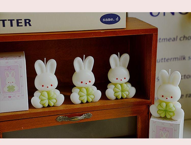 Three rabbit-shaped candles on a wooden shelf with a blurred background.
