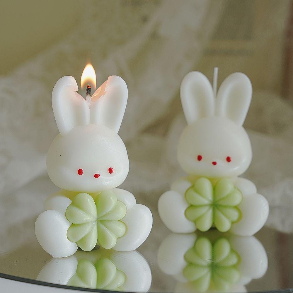 Two bunny-shaped candles with green bases on a reflective surface.