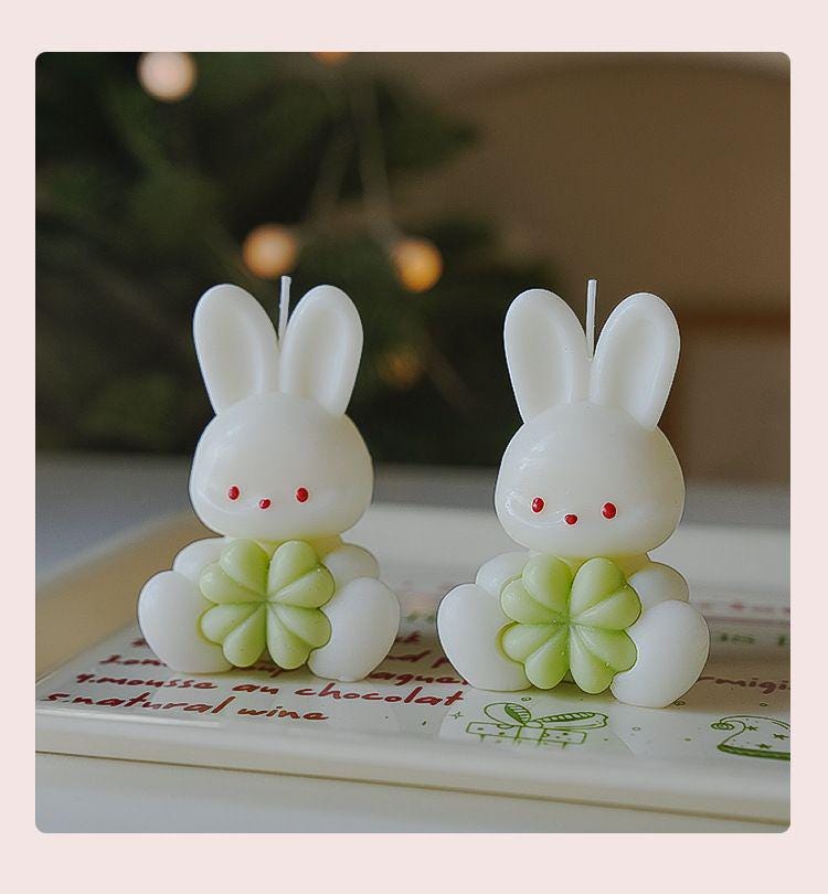 Two rabbit-shaped candles with green base on a book