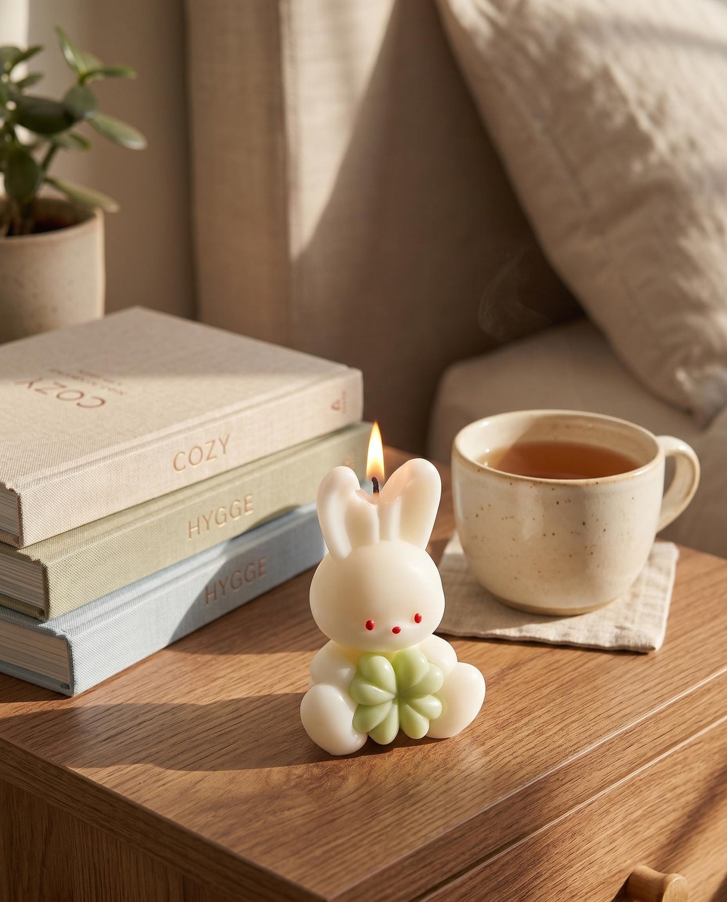Candle shaped like a rabbit with a cup of tea and books on a wooden table.